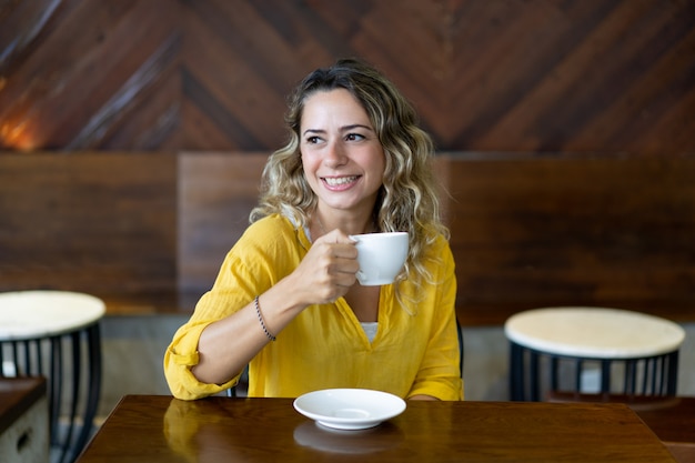 Heureuse jolie jeune femme buvant du thé au café