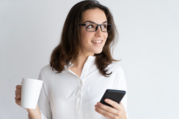 Heureuse jolie jeune femme tenant une tasse et un smartphone