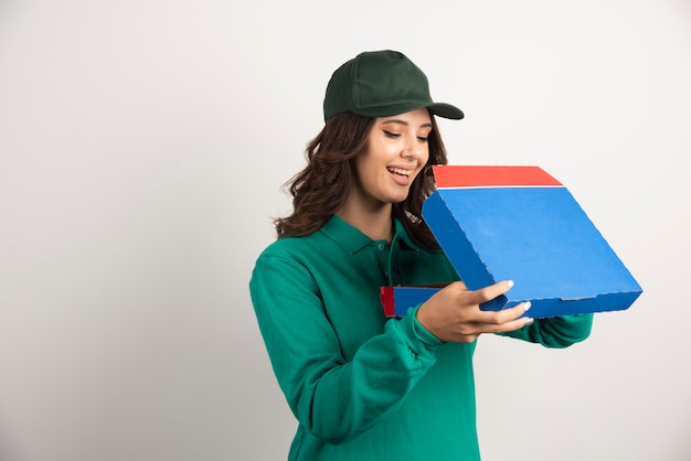 Heureuse livreuse ouvrant la boîte à pizza sur blanc.