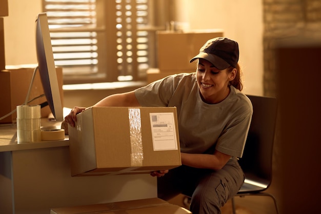 Heureuse livreuse préparant des boîtes en carton pour une expédition tout en travaillant au bureau