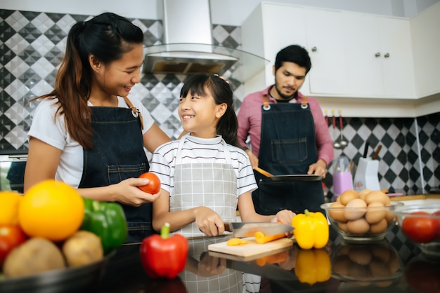 Heureuse maman enseigne à sa fille hacher des légumes préparant des ingrédients