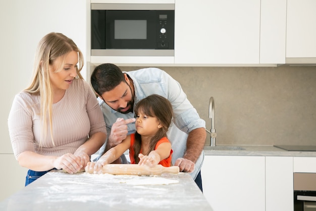 Heureuse maman et papa colorant le visage des filles avec des fleurs tout en cuisinant ensemble.