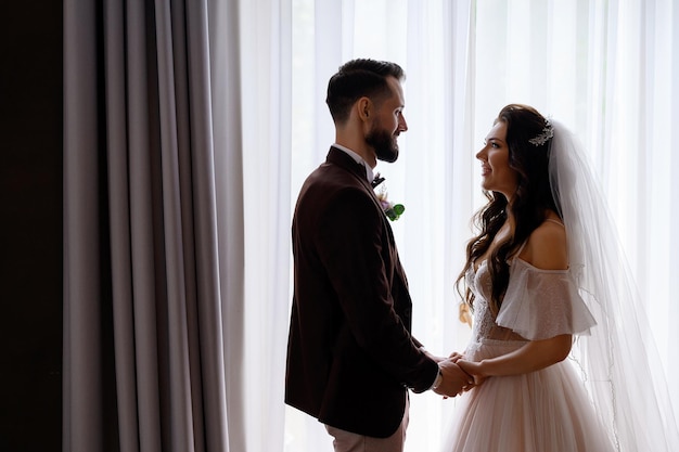 Heureuse mariée et le marié se regardant profiter du jour du mariage à l'intérieur