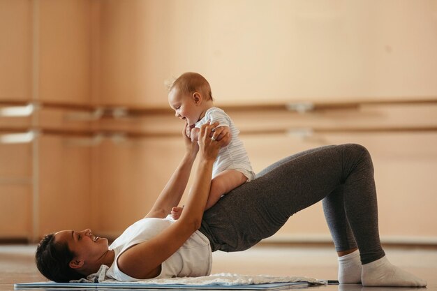 Heureuse mère athlétique s'amusant avec son bébé tout en faisant des exercices post-grossesse sur le sol