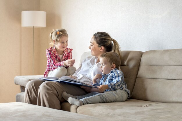 Heureuse mère caucasienne souriante avec enfants lisant un livre et s'amuser à la maison
