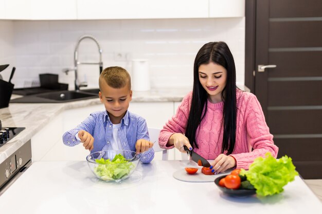 Heureuse mère de famille avec enfant fils prépare une salade de légumes à la maison