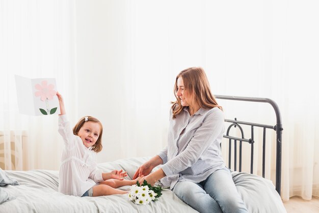 Heureuse mère et fille avec carte de voeux sur le lit