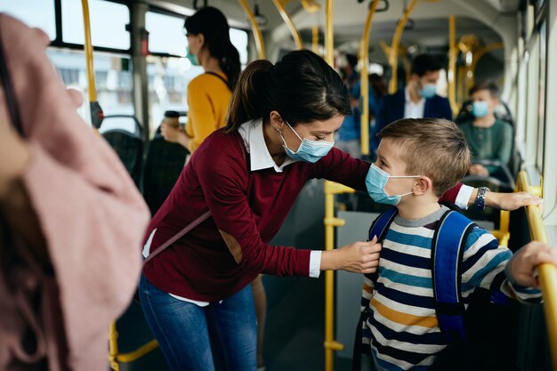 Heureuse mère et fils portant des masques pour se rendre à l'école en bus