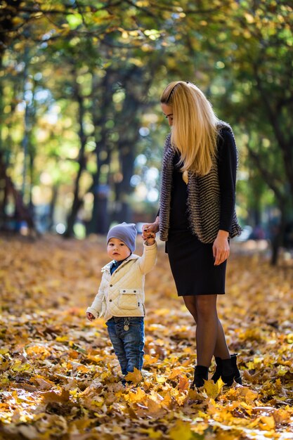 Heureuse mère jouant avec bébé dans le parc à l'automne. Kid souriant à maman sur les mains