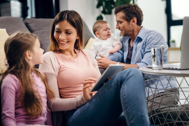 Heureuse mère et mère parlant tout en surfant sur le net sur le pavé tactile tandis que le père et le petit garçon sont en arrière-plan