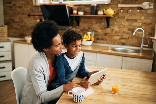 Heureuse mère noire et fils surfant sur le net sur le pavé tactile à la maison