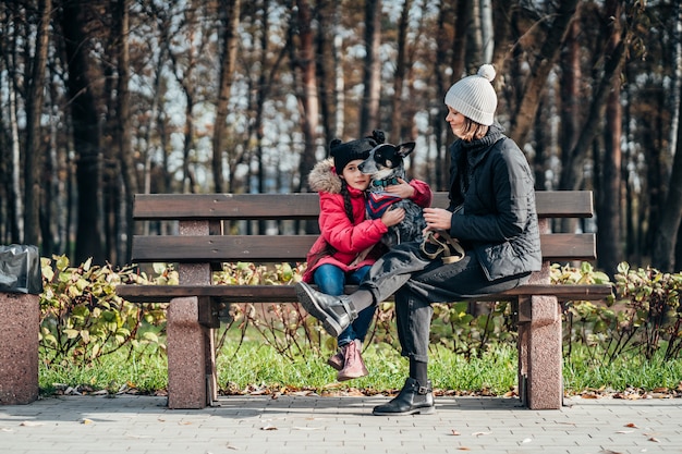 Heureuse mère et sa fille avec chien reposant sur un banc