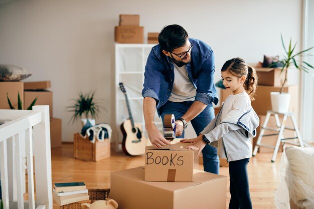 Heureuse petite fille et son père emballant des cartons tout en déménageant dans une nouvelle maison