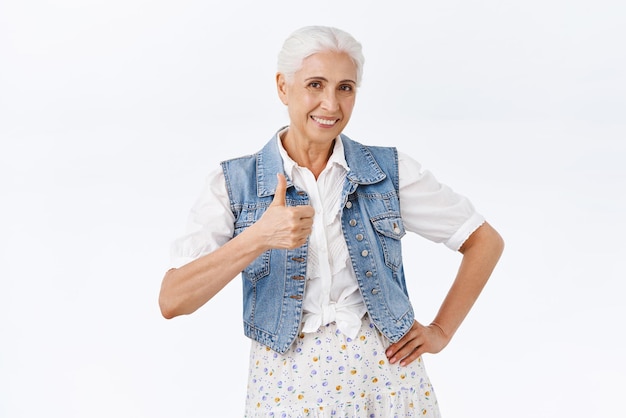 Heureuse satisfaite charmante mamie avec une expression heureuse souriante montrant le pouce levé taux ravi bon choix donner une opinion positive clin d'œil en acceptation d'accord avec vous fond blanc