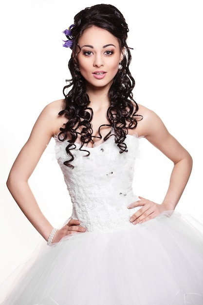 Heureuse sexy belle mariée brune fille en robe de mariée blanche avec coiffure et maquillage lumineux sur fond blanc