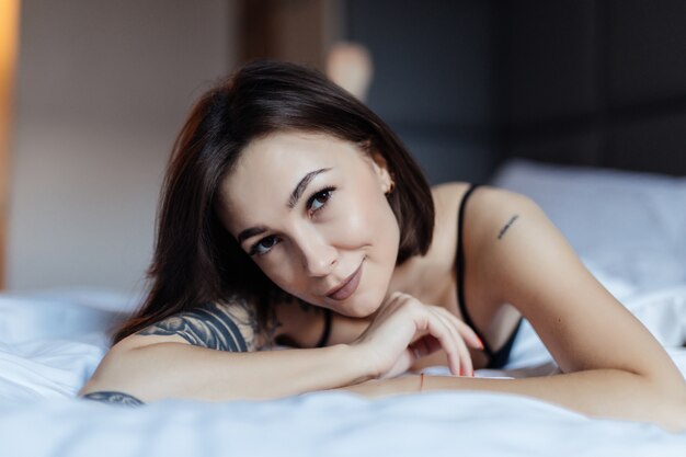 Heureuse souriante belle jeune femme au lit tôt le matin