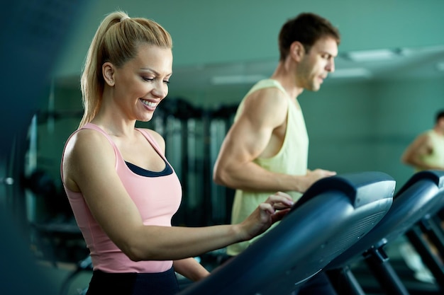 Photo gratuite heureuse sportive ajustant la vitesse sur un tapis roulant tout en faisant de l'exercice dans une salle de sport