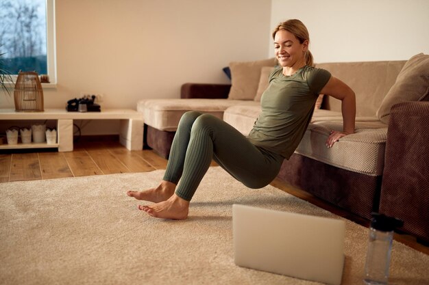 Heureuse sportive s'appuyant sur le canapé et pratiquant des trempettes de triceps pendant l'entraînement à domicile