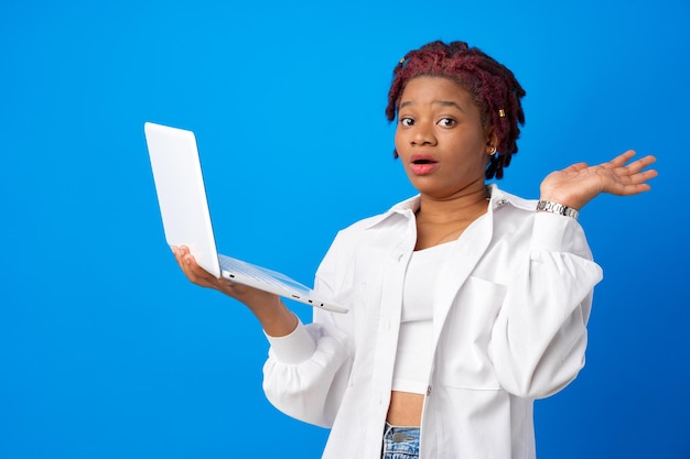 Heureuse surprise jeune femme afro-américaine tenant un ordinateur portable sur fond bleu