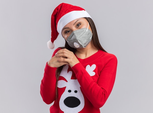 Heureuse tête inclinable jeune fille asiatique portant un chapeau de noël avec un pull et un masque médical tenant la main ensemble isolé sur fond blanc