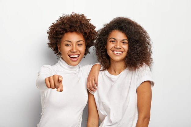 Heureuses et amicales, deux filles du millénaire ont des visages heureux, se tiennent l'une à côté de l'autre, pointent du doigt