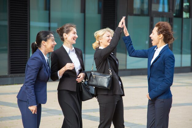 Heureuses dames d'affaires excitées qui donnent cinq. Femmes d'affaires portant des costumes réunis en ville, célébrant le succès. Concept de réussite et de travail d'équipe