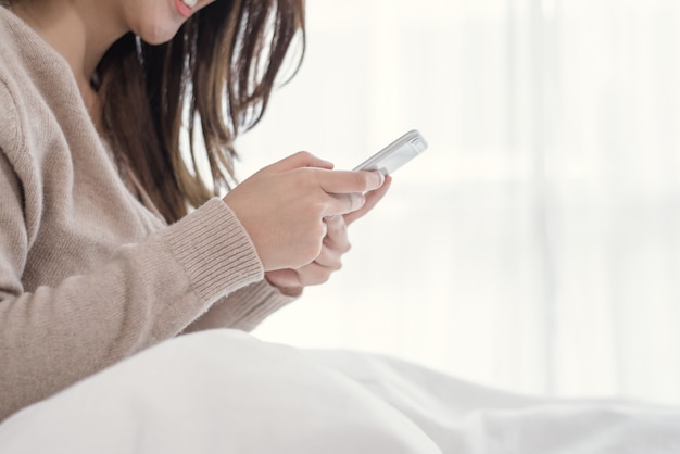 Heureuses femmes asiatiques utilisent un téléphone intelligent sur le lit le matin