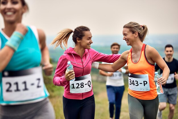 Heureuses femmes athlétiques se soutenant lors d'un marathon dans la nature