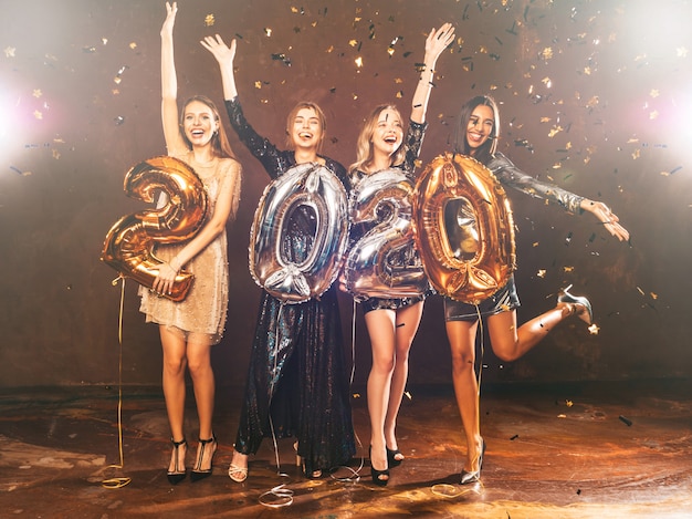 Heureuses filles magnifiques dans des robes de soirée sexy élégantes tenant des ballons d'or et d'argent 2020