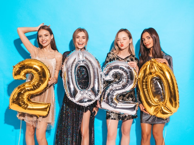 Heureuses filles magnifiques dans des robes de soirée sexy élégantes tenant des ballons d'or et d'argent 2020