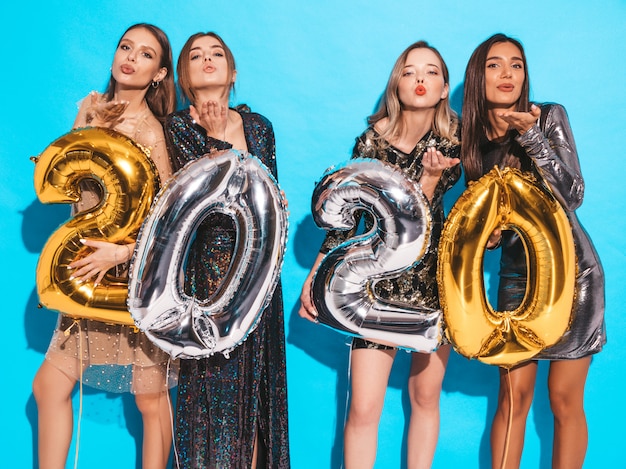 Heureuses filles magnifiques dans des robes de soirée sexy élégantes tenant des ballons d'or et d'argent 2020