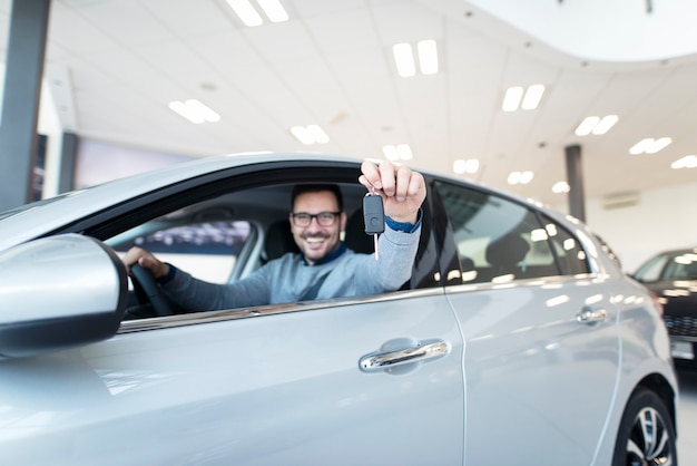 Heureux acheteur assis dans un nouveau véhicule et tenant des clés de voiture