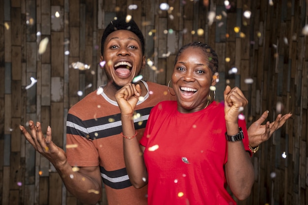 Photo gratuite heureux africains célébrant avec des confettis devant un mur en bois