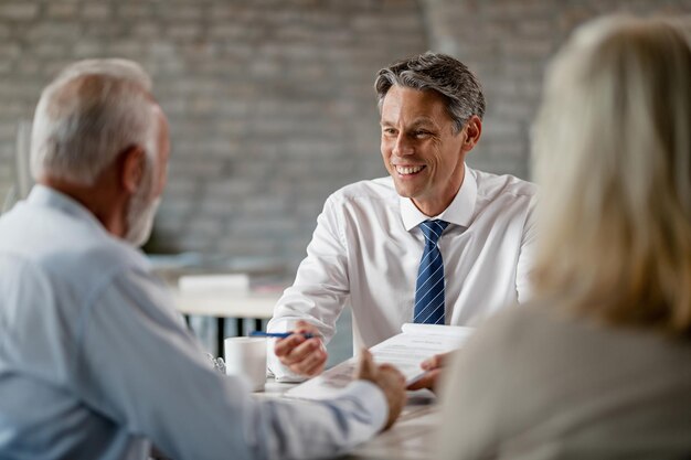 Heureux agent d'assurance communiquant avec des clients seniors tout en passant par la paperasse lors d'une réunion au bureau