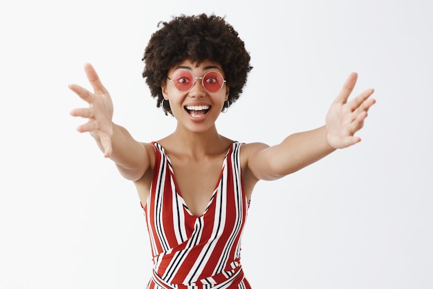 Photo gratuite heureux amical et heureux femme à la peau sombre émotive dans des lunettes et des vêtements élégants, tirant les mains vers un geste de bienvenue donnant un câlin ou un câlin