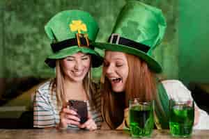 Photo gratuite heureux amies célébrant st. patrick's day ensemble au bar avec smartphone