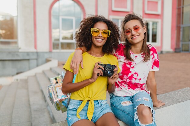 Heureux amis de jeunes filles souriant assis dans la rue avec appareil photo, les femmes s'amusant ensemble