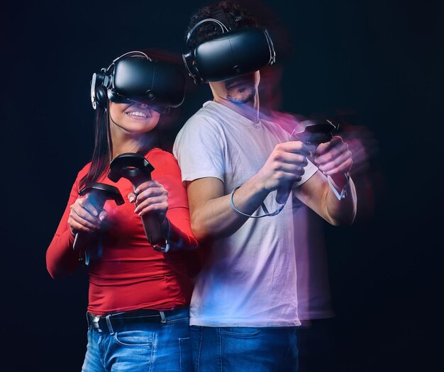 Heureux amis jouant à des jeux vidéo portant des lunettes de réalité virtuelle avec des contrôleurs. Isolé sur fond sombre. Photo avec effet de lumière.