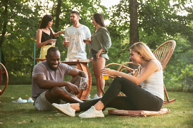 Heureux amis manger et boire des bières au dîner barbecue au coucher du soleil