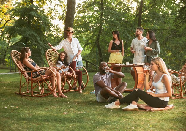 Heureux amis manger et boire des bières au dîner barbecue au coucher du soleil