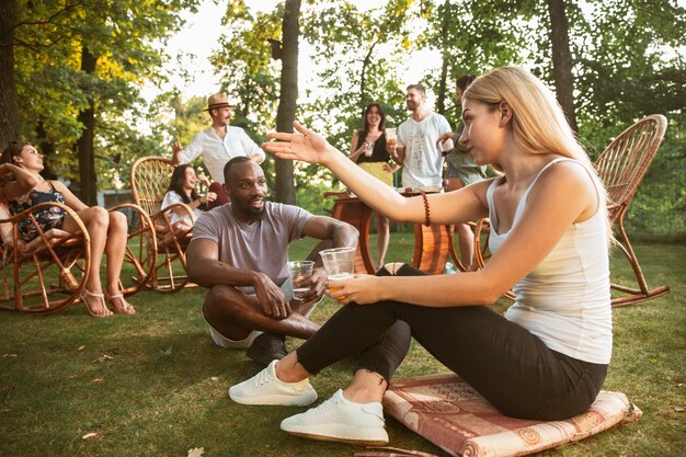 Heureux amis manger et boire des bières au dîner barbecue au coucher du soleil