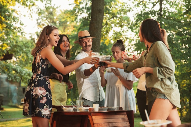 Heureux amis manger et boire des bières au dîner barbecue au coucher du soleil