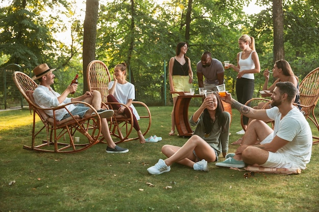 Heureux amis manger et boire des bières au dîner barbecue au coucher du soleil