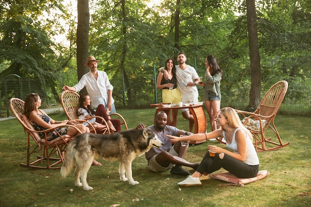 Heureux amis manger et boire des bières au dîner barbecue au coucher du soleil