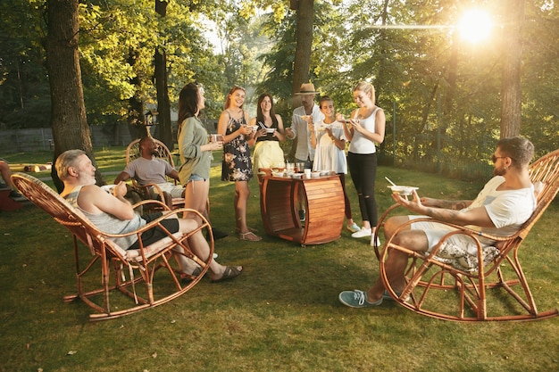 Heureux amis manger et boire des bières au dîner barbecue au coucher du soleil