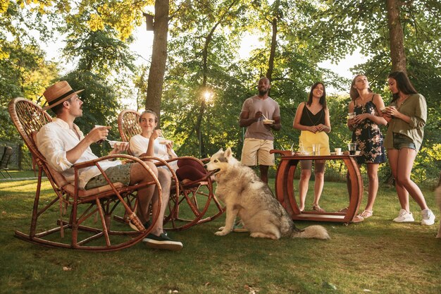 Heureux amis manger et boire des bières au dîner barbecue au coucher du soleil