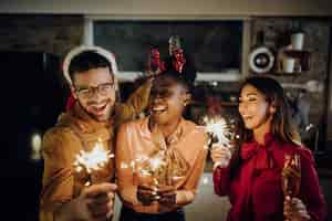 Photo gratuite heureux amis s'amusant avec des cierges magiques lors de la fête du nouvel an à la maison