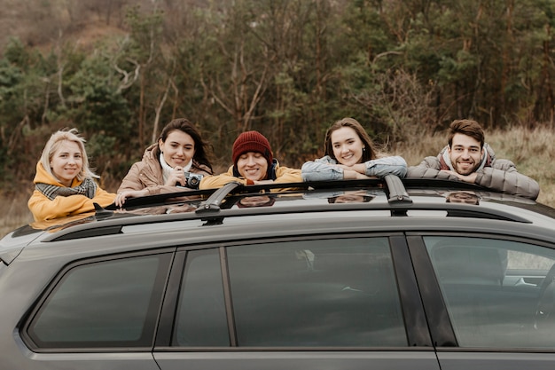 Photo gratuite heureux amis s'appuyant sur la voiture