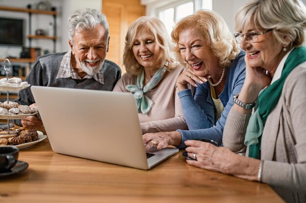 Heureux amis seniors appréciant tout en regardant ensemble quelque chose sur un ordinateur portable à la maison