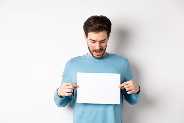 Heureux barbu lisant une bannière sur une feuille de papier vierge, montrant le logo, debout sur fond blanc